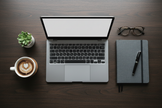 Gray laptop flat lay with notebook and coffee on dark wood desk